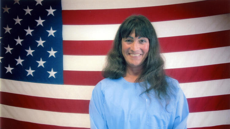 Photo of transgender woman Shiloh Heavenly Quine. She stands in front of an american flag and is smilng