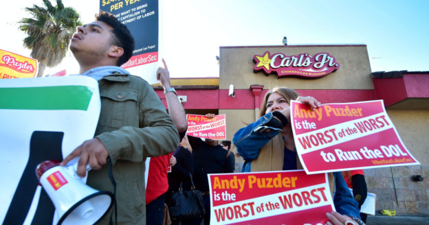 Protesters outside of a Carl's Jr hold signs that read "Andy Puzder is the worst of the worst" (Credit: rSS Food).